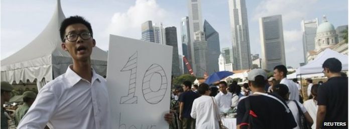 Man with a sign saying queue length is ten hours in Singapore (27 March 2015)