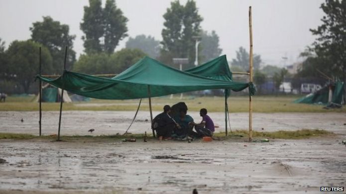 Earthquake victims sit under a makeshift shelter as it rains in Kathmandu (30 April 2015)