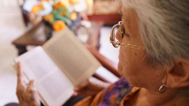 Una mujer mayor lee un libro.