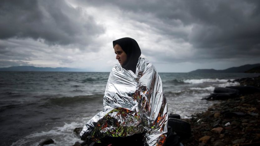 A woman tries to warm up herself using a thermal blanket provided by volunteers after arriving on a dinghy from a Turkish coast to the northeastern Greek island of Lesbos, Saturday, Oct. 24, 2015