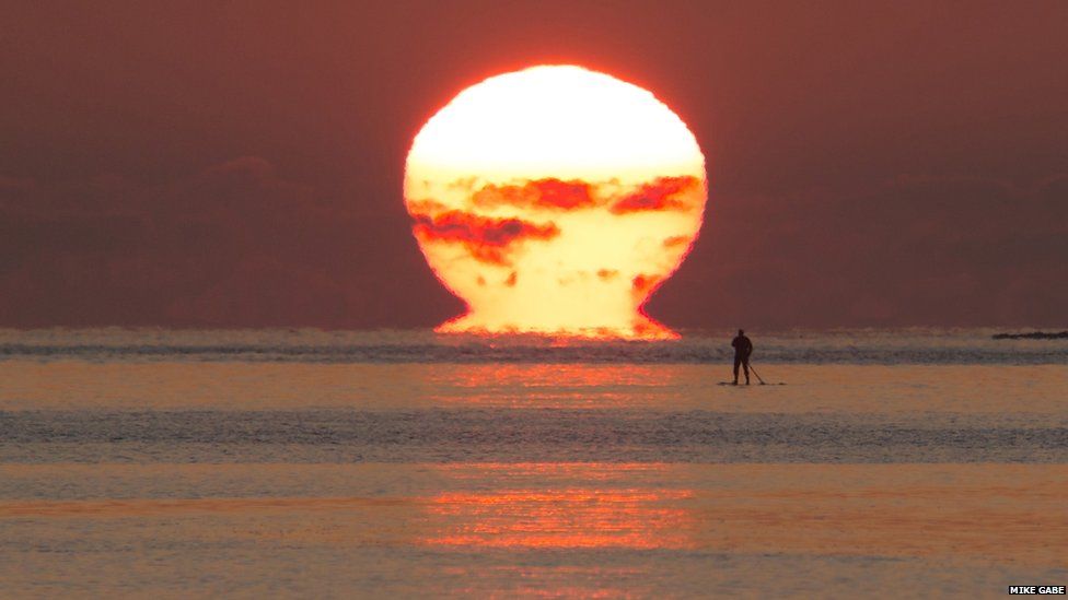 A man on a paddleboard in the sea as the sun sets