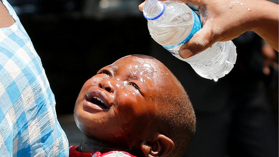 A woman pours water over a child affected by teargas after clashes between police and street vendors in central Harare, Zimbabwe,