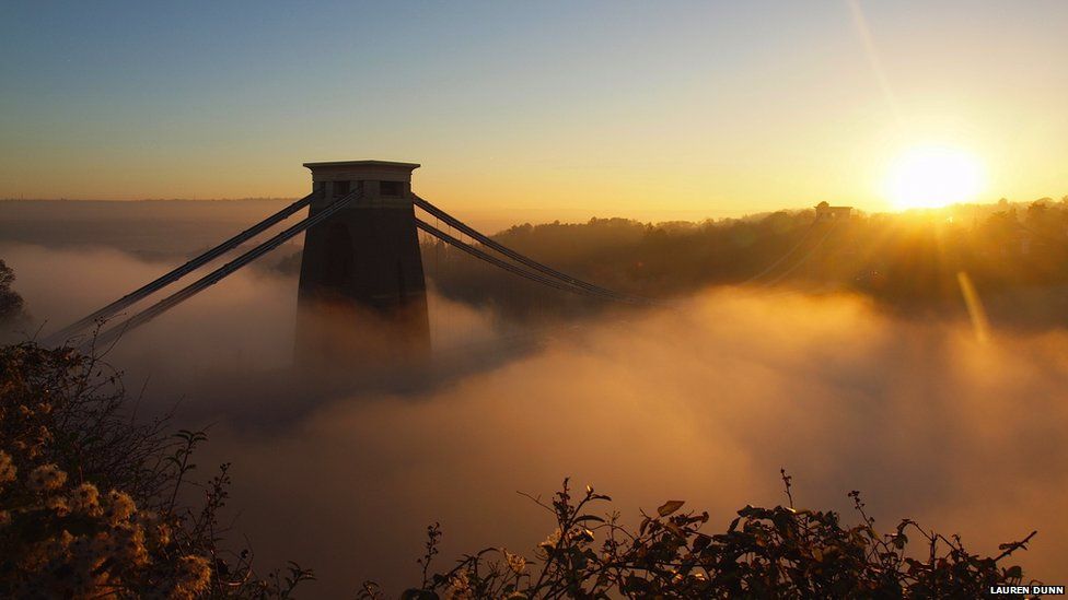A suspension bridge is almost completely shrouded in mist at sunset