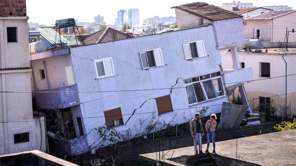 People stand in front of a collapsed building in the town of Durres, western Albania 27 November 2019
