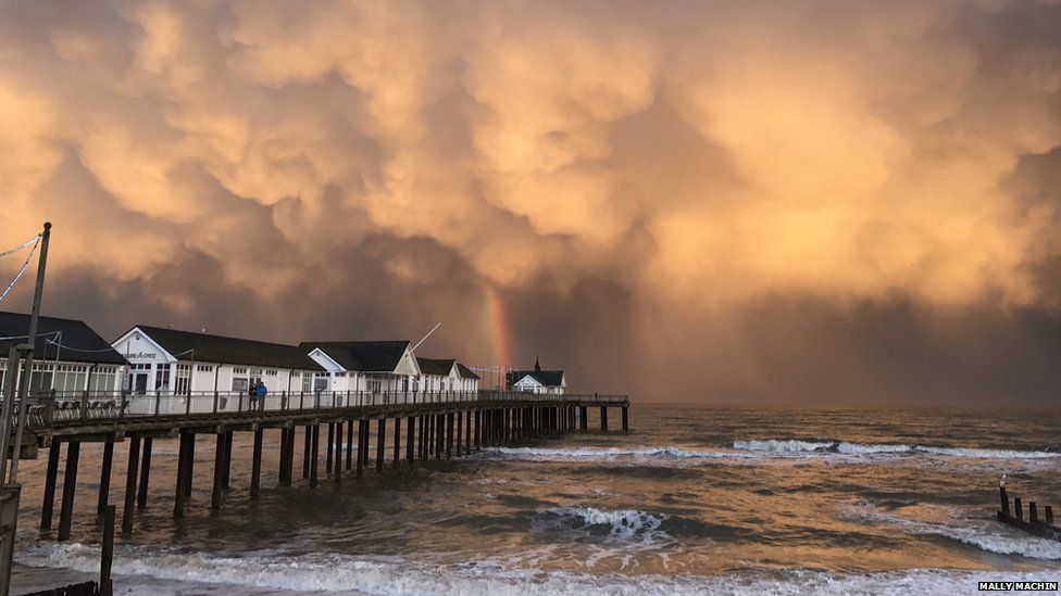 Storm clouds and a rainbow by a pier