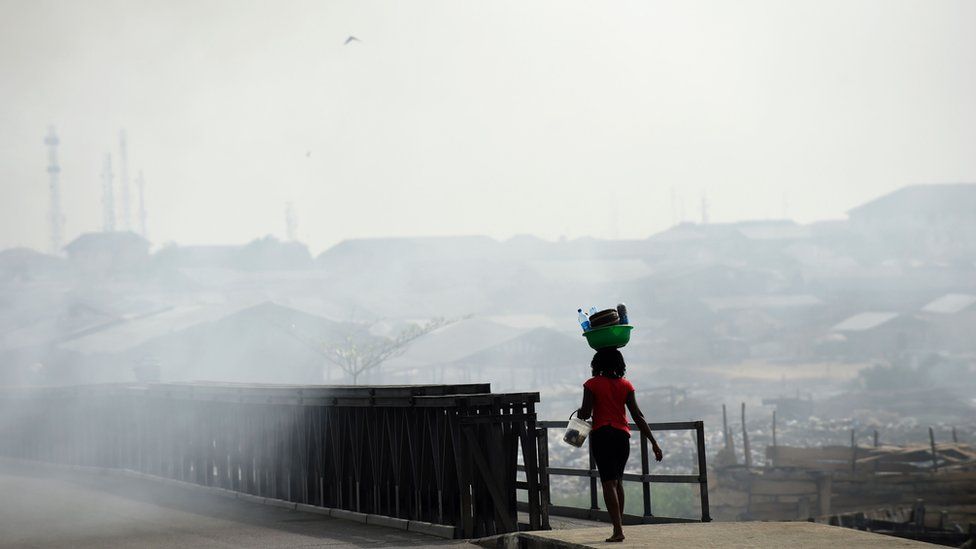 A woman walks through the smoke emitted from a dump