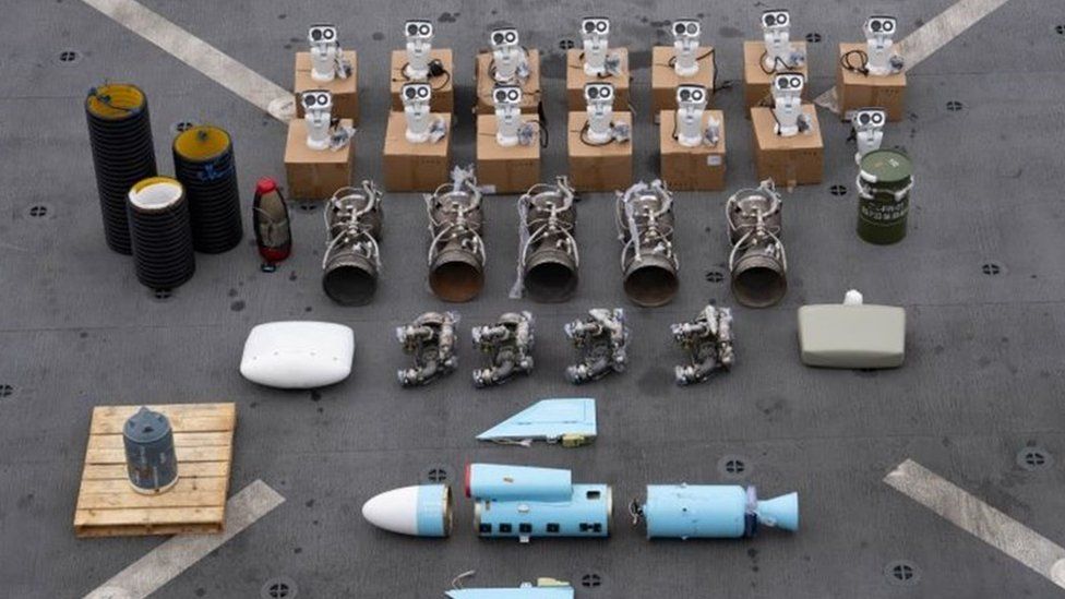 Weapons seized by the US from a ship near the coast of Somalia, lined up on the deck of a ship. It shows a number of deconstructed parts, with a missile shown in multiple parts at the bottom of the screen.