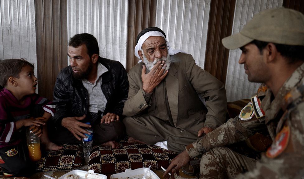 A group of civilians sit, eat and smoke cigarettes with Iraqi soldiers in eastern Mosul (1 November 2016)