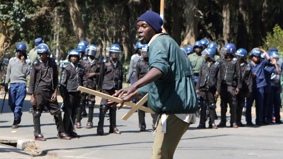 A protester holding a wooden cross in front of police in Harare, Zimbabwe - Wednesday 3 August 2016