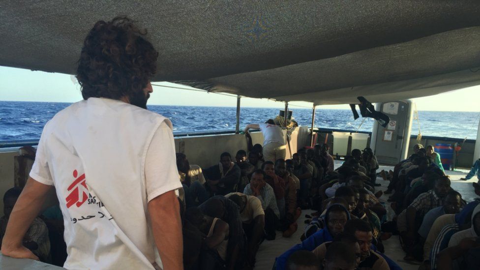 A Médecins Sans Frontières worker looks on at a group of rescued refugees