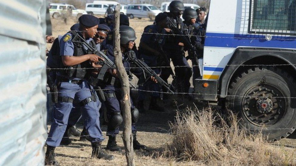 Police officers look at protesting miners near a platinum mine in Marikana on August 16, 2012
