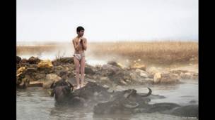 Un muchacho de un pueblito congelado está parado al ladode una piscina natural de aguas termales, una foto