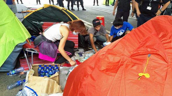 香港金钟道上“占领中环”示威者在警员监视下收拾急救用品（BBC中文网图片14/10/2014）