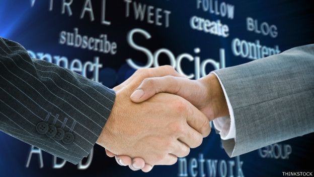 Dos personas que se dan la mano con un fondo de palabras asociadas a las redes sociales