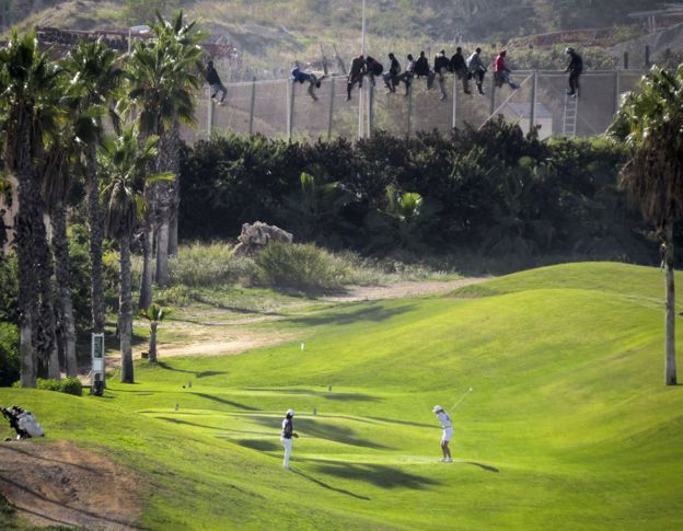 Inmigrantes permanecen sobre la valla de Melilla, junto a un campo de golf