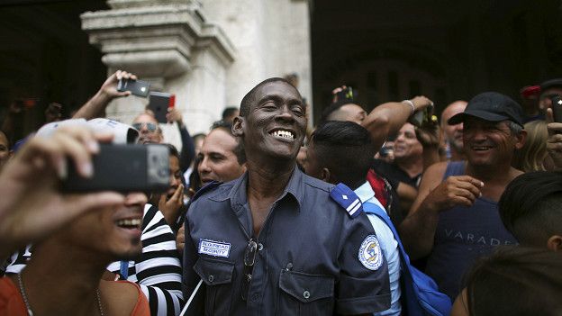 Un policía del gobierno cubano sonríe junto a la multitud mientras esperaban que el presidente Obama pasara por Centro Habana