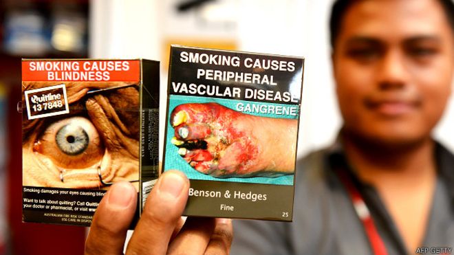 Vendedor de cigarrillos en Australia mostrando dos paquetes con imágenes gráficas