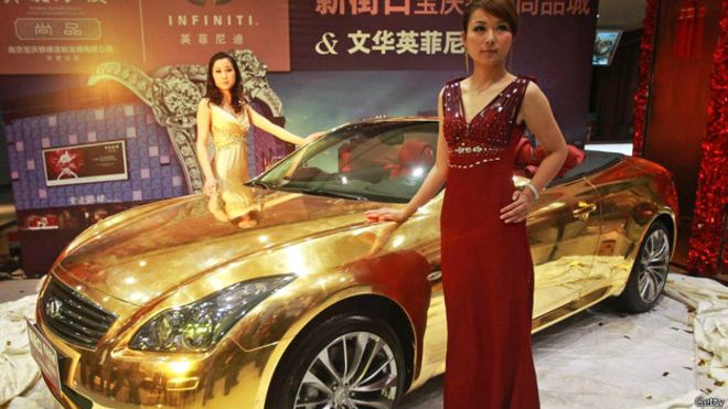 Un auto dorado en exhibición, con unas modelos chinas