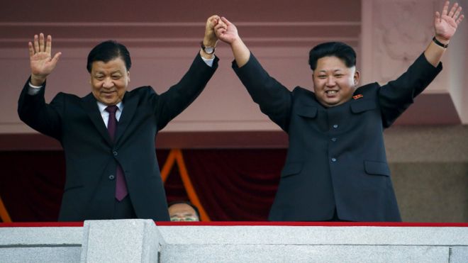 金正恩高举刘云山（左）的手向检阅队伍挥手（10/10/2015）