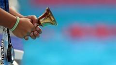 hands of a volunteer holding a bell on the edge of a pool