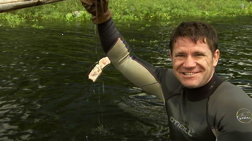 Steve Backshall standing in a river holding a bone