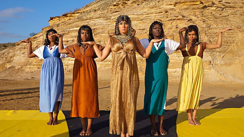 Cleopatra and dancers dance in front of a pyramid