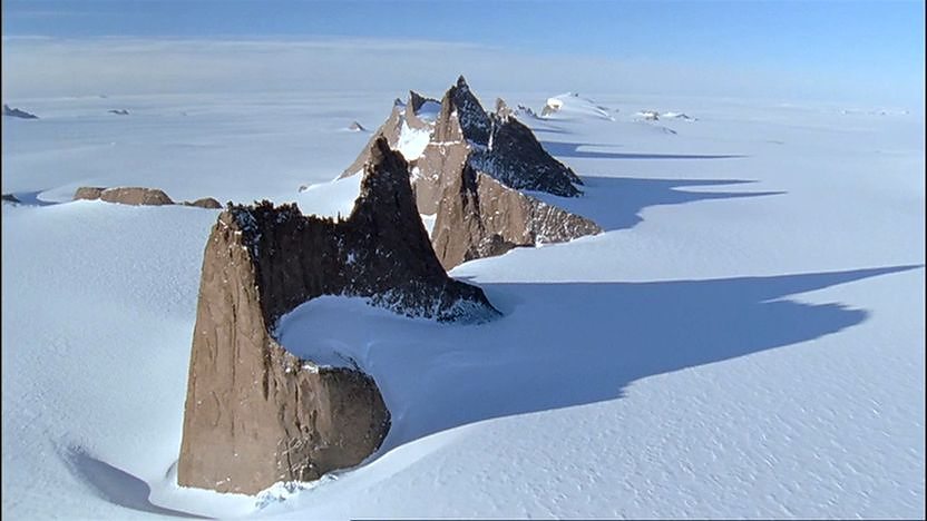 Rocky peaks, standing up and out from thick snow in the antarctic.