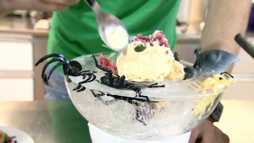 A spoon going into an ice bowl filled with frozen ice cream with a spider coming out with it.