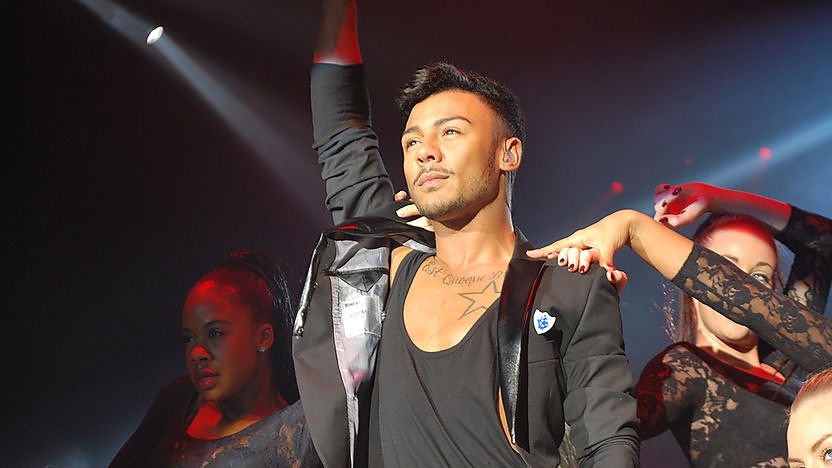Marcus Collins performing in a red blazer wearing a blue peter badge.
