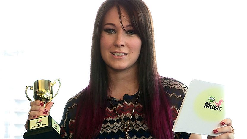 Stacey, keyboardist and vocalist is Clement Marfo and the Frontline holding the CBBC Music Pop Champions trophy and CBBC Music question cards.