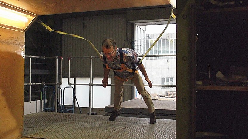 Leo leans into strong generated winds wearing a safety harness
