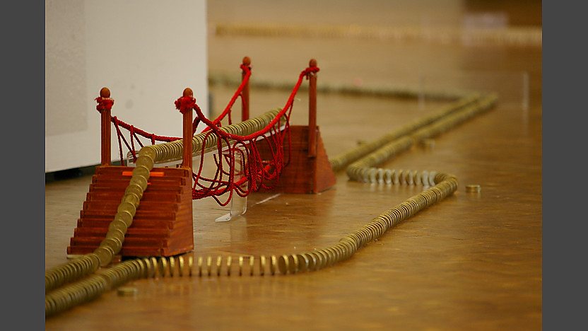 Pound coins stood up like dominoes over a model rope bridge