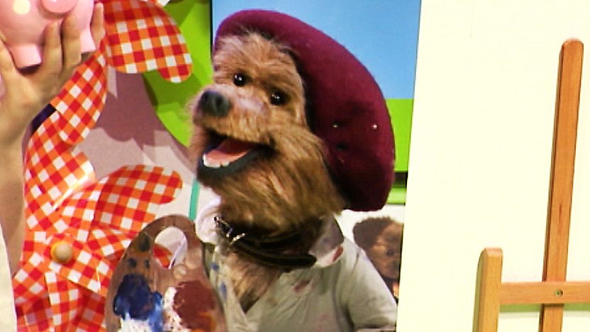 Hacker T Dog wearing a beret and holding a paint brush in front of a canvas.