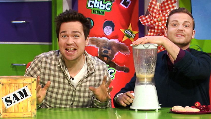 Sam Nixon pulling a funny face while Mark Rhodes blends a mixture in a blender in the CBBC Office.