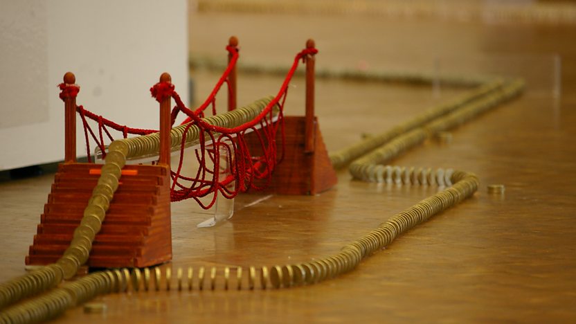 Pound coins stood up like dominoes over a model rope bridge