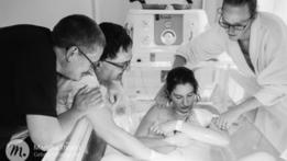La madre sostiene a su bebé en la tina mientras los padres de ella y su esposo lo miran