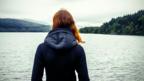 A woman feeling homesick looking out on a lake.