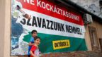 Hungarian Roma boys walk in front of the Hungarian government's poster regarding referendum on EU migrant quotas in Budapest