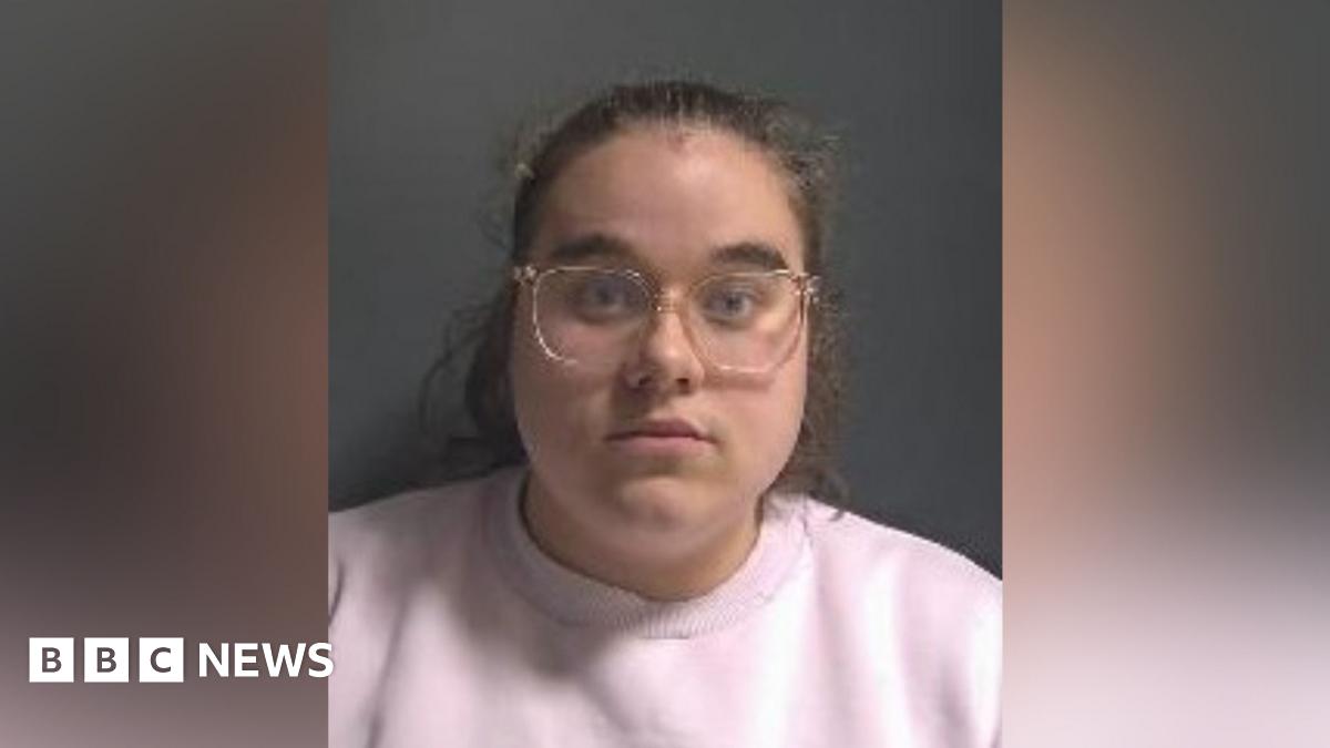 Zara Lancashire: a woman with pulled back brown hair wearing pale-rimmed glasses and a pink round-necked top.