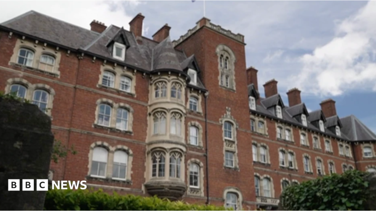 The image shows a large, heritage brick building with perhaps gothic features around windows and a tall central column in the centre of the school.