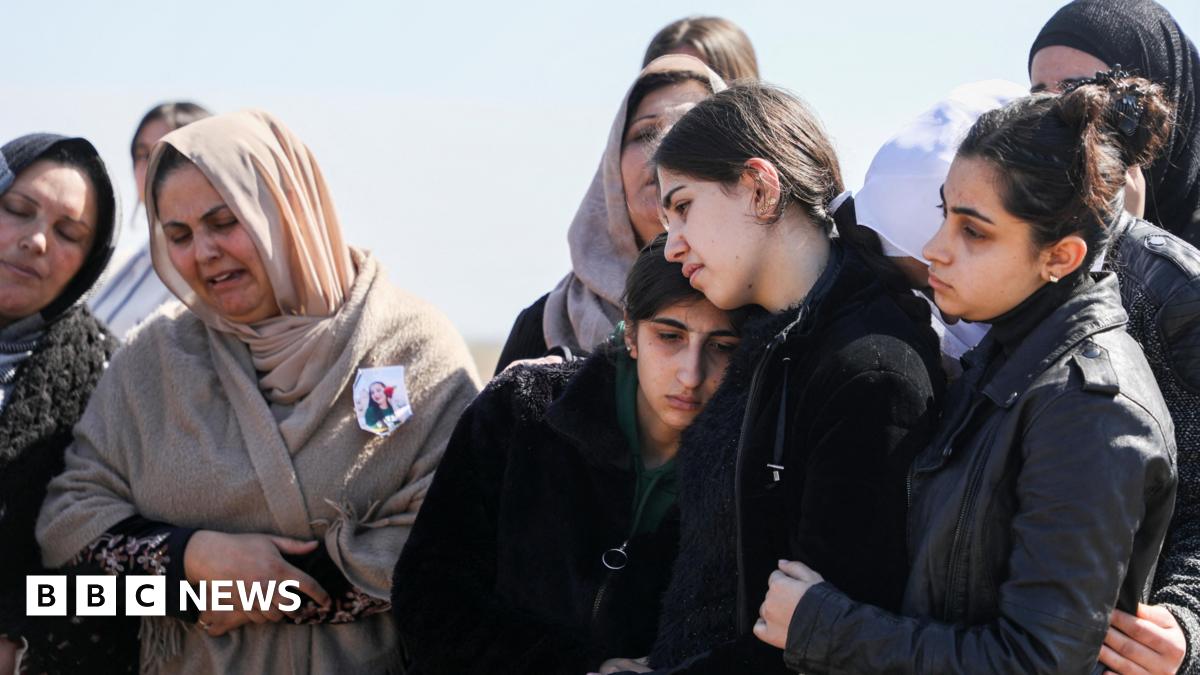 Female mourners at a funeral in Latakia, dressed in grey and black and some with headscarves, cry and comfort each other