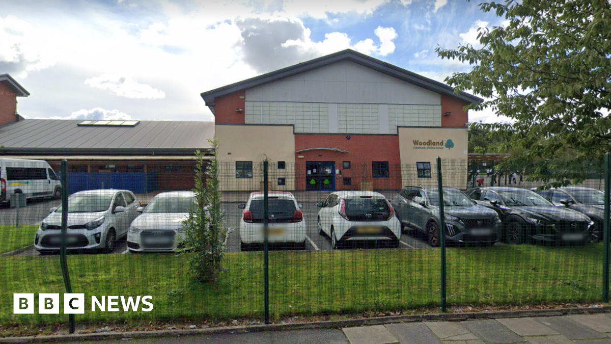 A street view of Woodland Community Primary School. It is a single story building with a car park, and a playground.