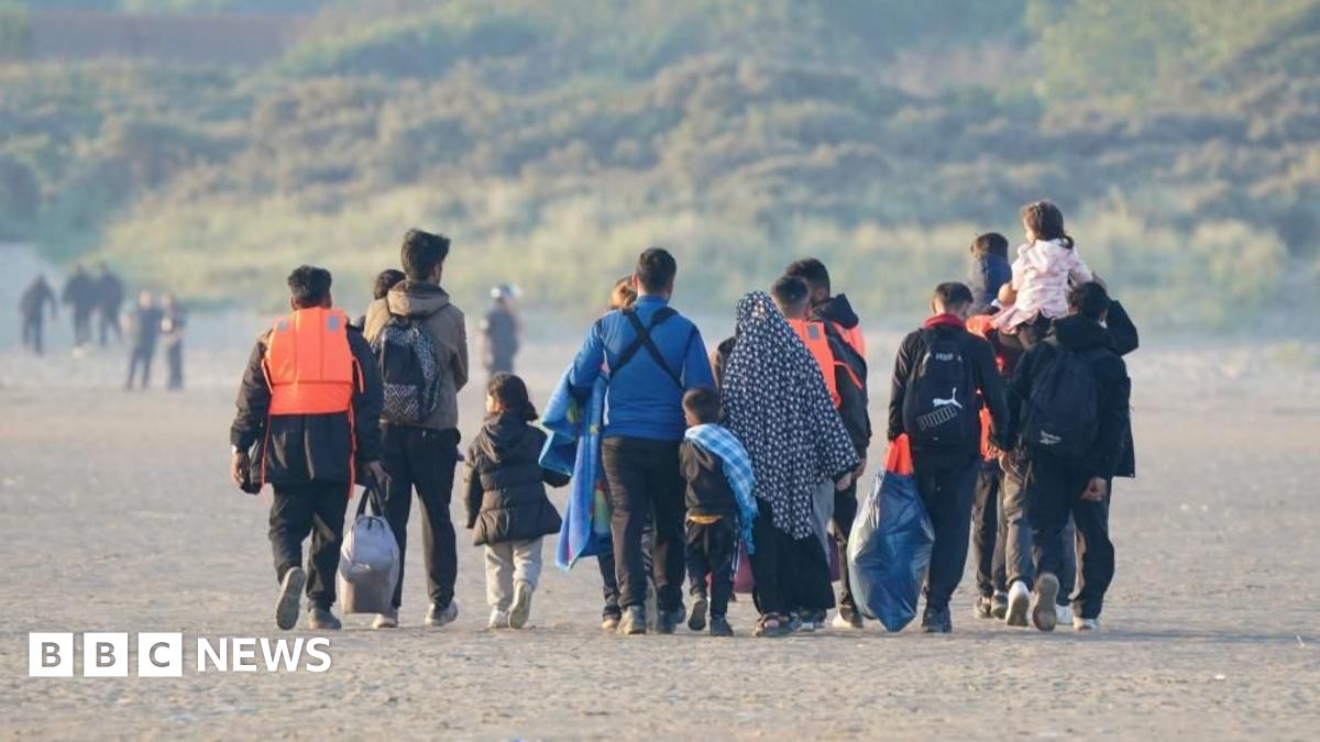 A group of people, some wearing life jackets, walking along a beach