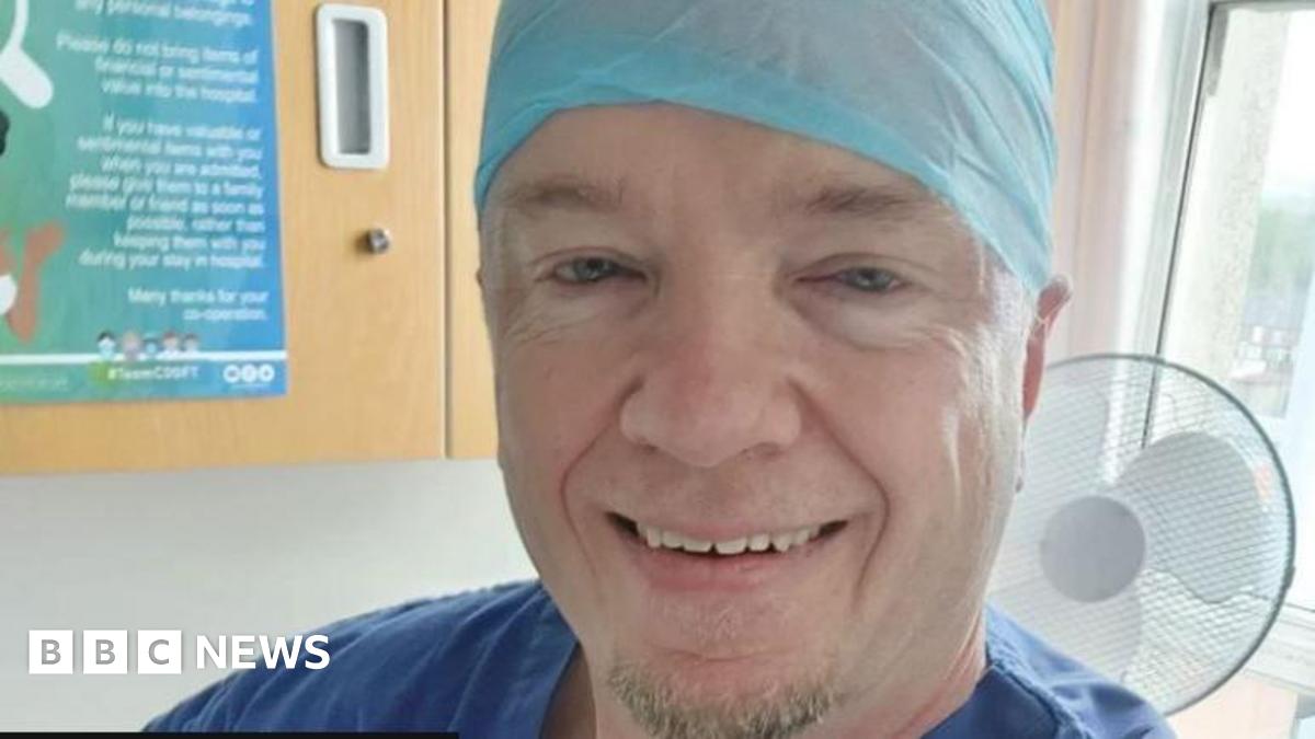 Robert Albon, who appears to be in a medical facility. He has a blue top, possibly a gown, that is just visible and a blue head covering as you might see in a surgical setting. He is smiling and has a small amount of short light coloured beard growth o...
