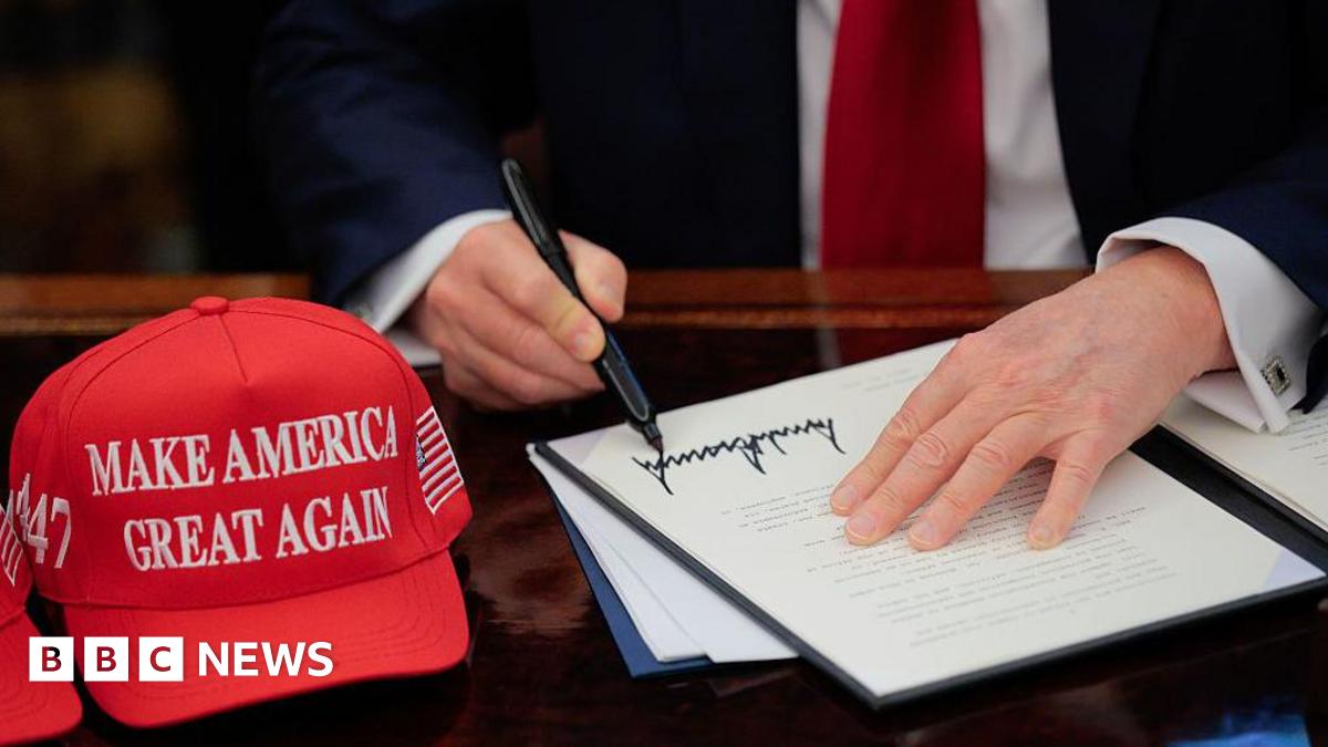 US President Donald Trump signs an executive order in the Oval Office at the White House in Washington, DC on 23 April 2025.  A red baseball hat embroidered with "Make America Great Again" in white thread sits to the left of the document, which shows T...