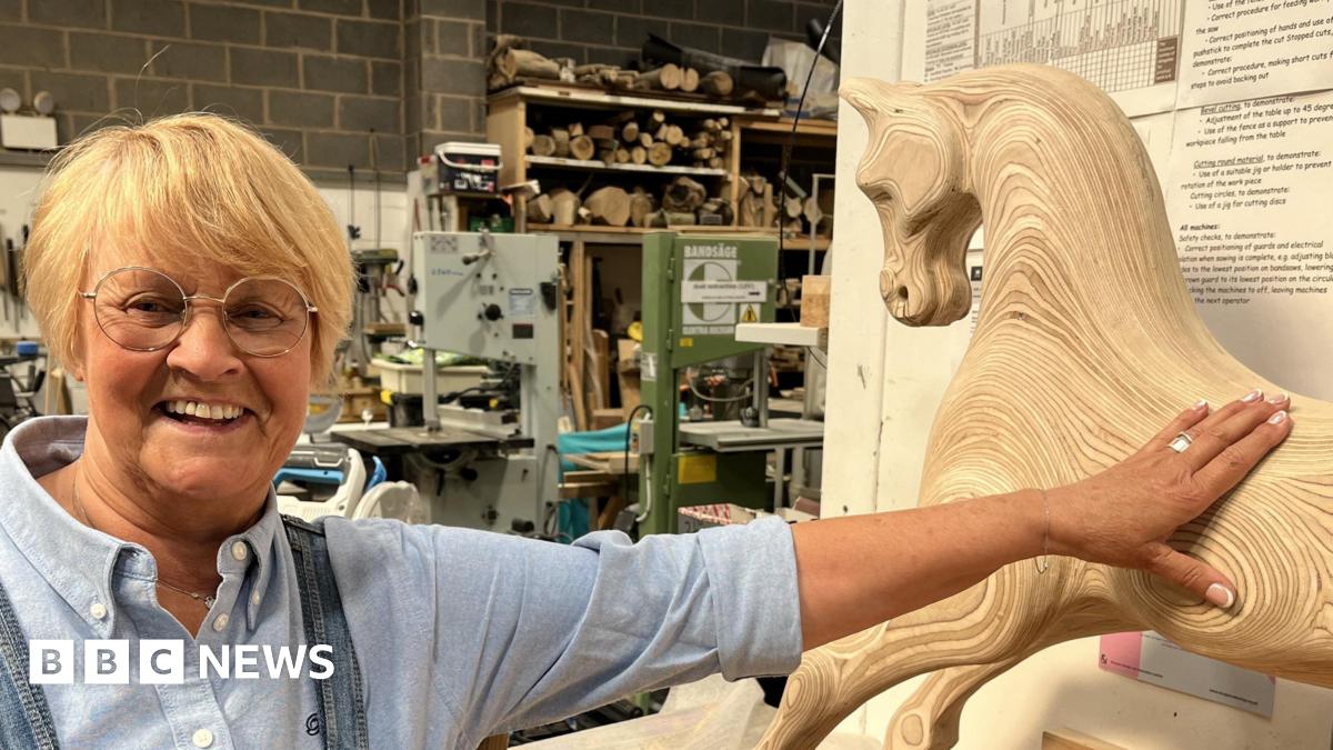 Brenda, wearing dungarees, next to a wooden rocking horse she's created 