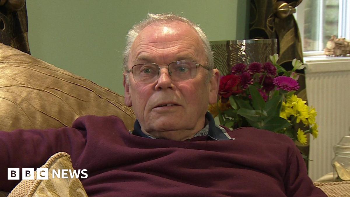 Alan Knight sits on his sofa giving a TV interview. He has light grey hair and glasses.