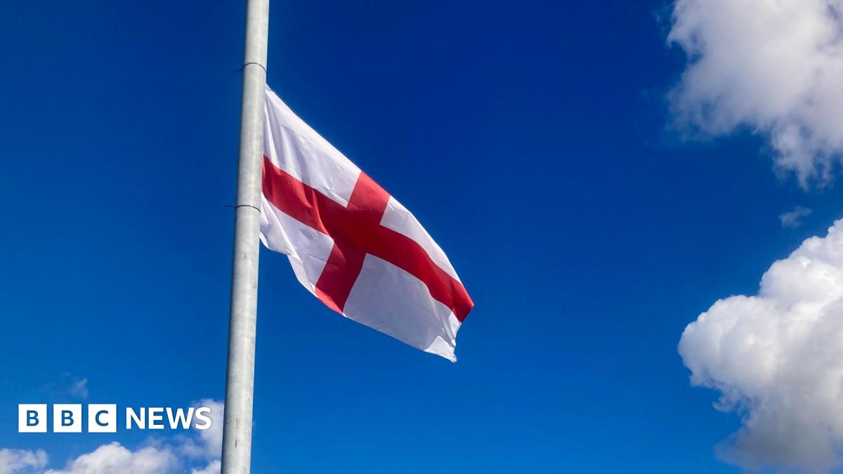 An England flag attached to a lamppost, set against a blue sky with light-coloured clouds.
