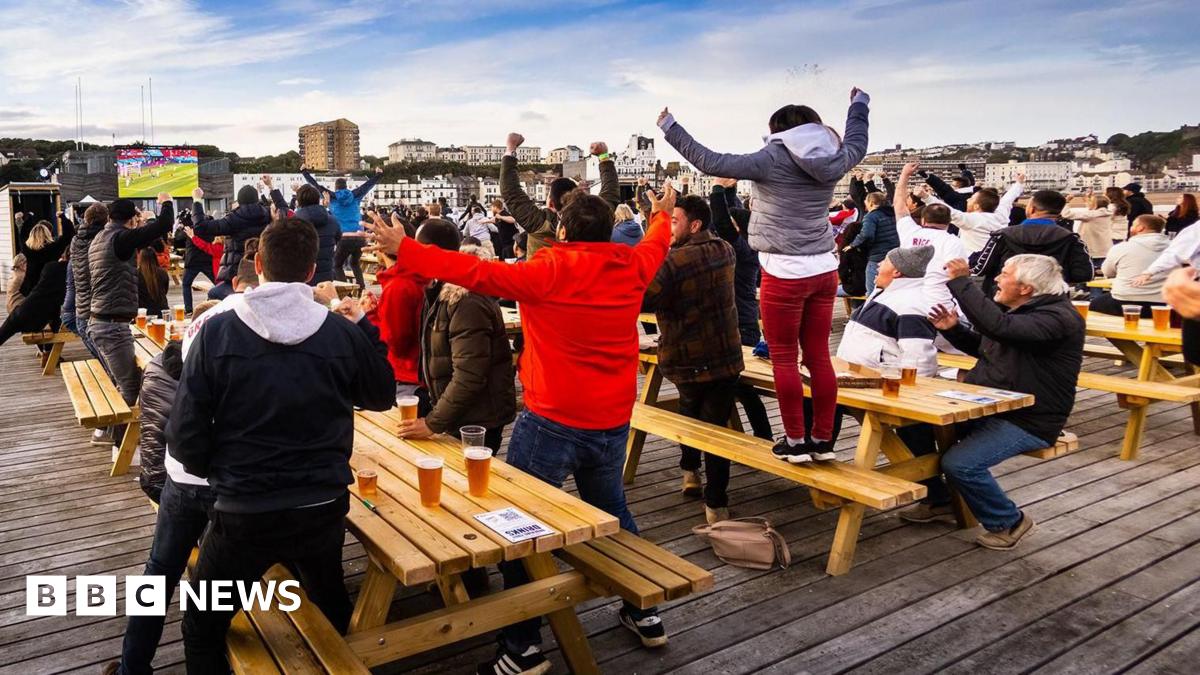 People celebrating on Hastings Pier with screen at far end showing football match 