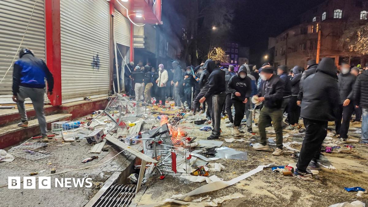 A group of people in face masks and hoods gather around burning debris outside shuttered shops in Kermanshah on Thursday.
